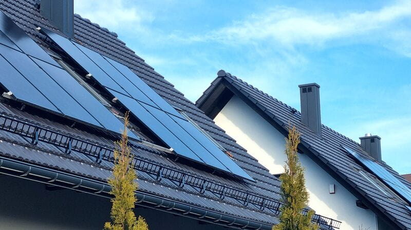 dwa, szare dachy, na których zamontowane są panele fotowoltaiczne