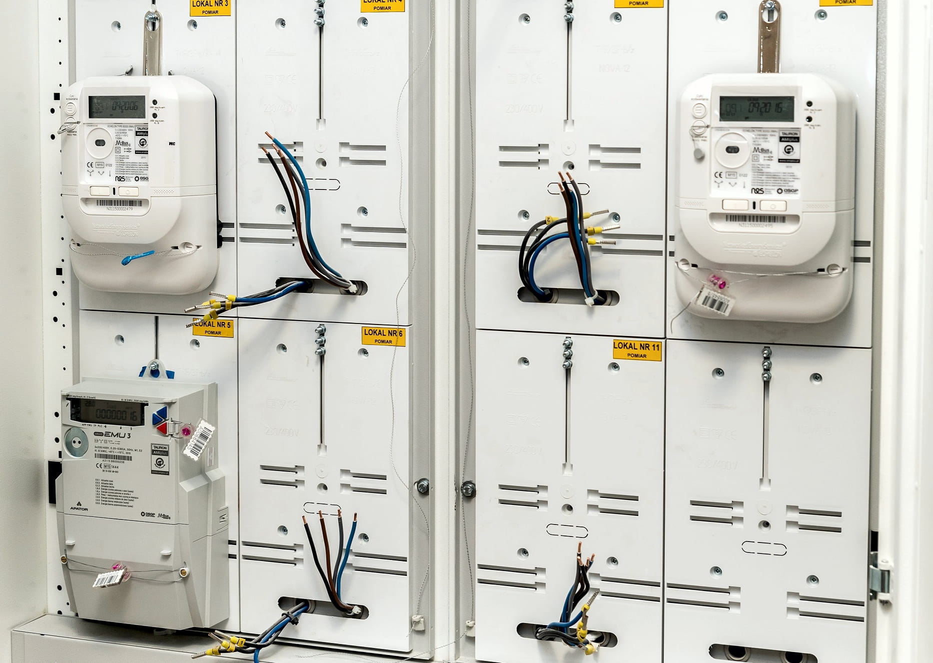 trzy białe liczniki energii elektrycznej umieszczone w szafce licznikowej domu wielorodzinnego